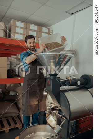 Entrepreneur pouring raw coffee beans into a modern roasting machine. 90359047