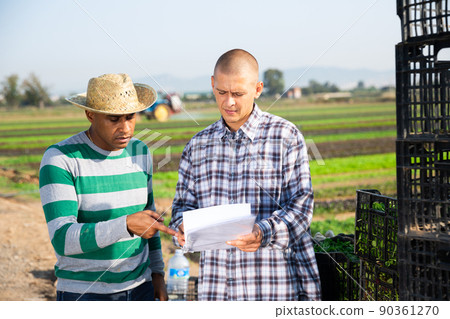 Farmers discussing documents near boxes with vegetables on field Farmers discussing documents near boxes with vegetables on field 90361270