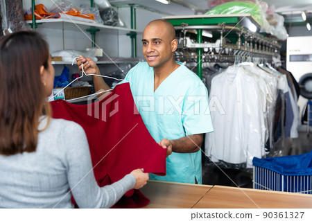 Male employee with client in modern laundry, returning clothing after cleaning 90361327