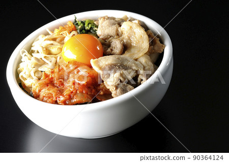 A bibimbap bowl with lots of ingredients such as bean sprouts, kimchi, and pork is shot on a black background. 90364124
