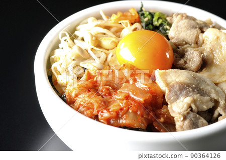A bibimbap bowl with lots of ingredients such as bean sprouts, kimchi, and pork is shot on a black background. 90364126
