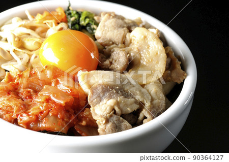A bibimbap bowl with lots of ingredients such as bean sprouts, kimchi, and pork is shot on a black background. 90364127