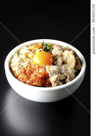 A bibimbap bowl with lots of ingredients such as bean sprouts, kimchi, and pork is shot on a black background. 90364128