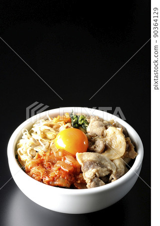 A bibimbap bowl with lots of ingredients such as bean sprouts, kimchi, and pork is shot on a black background. 90364129