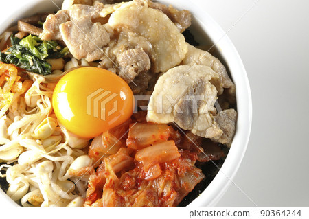 一個包含很多配料的石鍋拌飯碗的鳥瞰圖,例如白色背景上的豆芽、泡菜和豬肉。 一個包含很多配料的石鍋拌飯碗的鳥瞰圖,例如白色背景上的豆芽、泡菜和豬肉。 90364244
