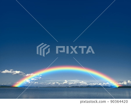 Rainbow on dark blue sky and white cloud on lake and line of tree and tiny mountain Rainbow on dark blue sky and white cloud on lake and line of tree and tiny mountain 90364420