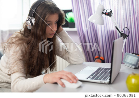 A young brunette is homeschooling remotely via the internet and laptop. 90365081