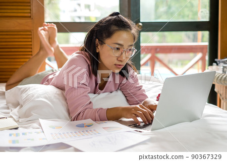 work from home, a young Asian woman who works in finance at home calculates financial graphs showing the results of his investments, planning the steps of his business growth work from home, a young Asian woman who works in finance at home calculates financial graphs showing the results of his investments, planning the steps of his business growth 90367329