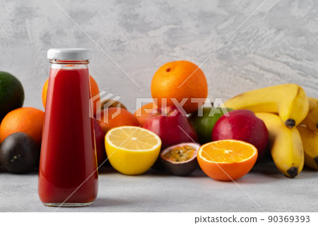 Various fruits and freshly squeezed fruits juice in bottle on gray background Various fruits and freshly squeezed fruits juice in bottle on gray background 90369393
