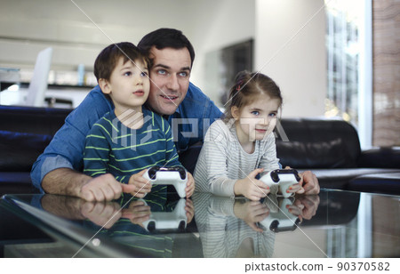 Smiling young man playing videogame together with son and daughter in modern living room 90370582