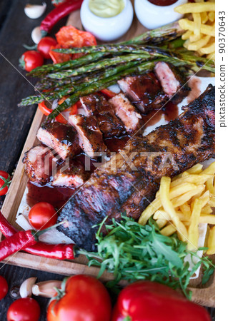 Barbecue pork ribs on wooden serving board on picnic table outdoors 90370643