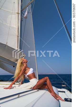Beautiful young blond woman in bikini sitting on catamaran at sunny summer day 90370697