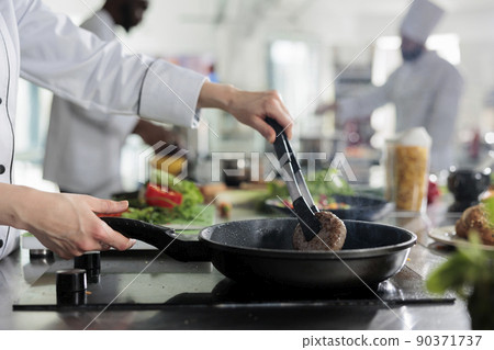 Master chef hands cooking beef patty in hot pan while cooking gourmet dish for dinner service. Skilled food industry worker frying minced meat in restaurant professional kitchen. Master chef hands cooking beef patty in hot pan while cooking gourmet dish for dinner service. Skilled food industry worker frying minced meat in restaurant professional kitchen. 90371737