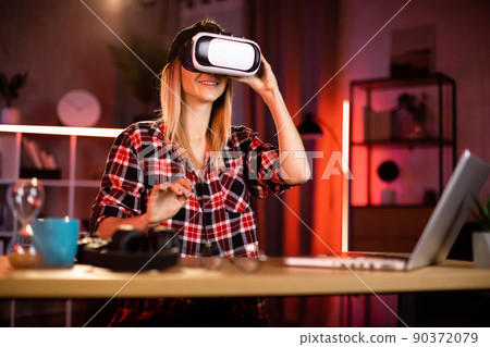 Caucasian woman in headset touching virtual screen while sitting at desk with wireless laptop Caucasian woman in headset touching virtual screen while sitting at desk with wireless laptop 90372079
