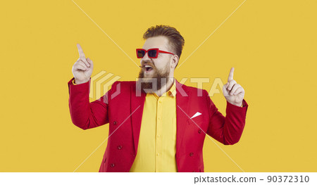 Cheerful and stylish young extravagant chubby man having fun and dancing on yellow background. Cheerful and stylish young extravagant chubby man having fun and dancing on yellow background. 90372310