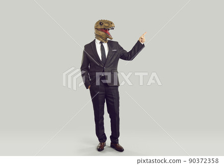 Funny businessman with dinosaur head showing finger on copy space, isolated on gray background. Funny businessman with dinosaur head showing finger on copy space, isolated on gray background. 90372358