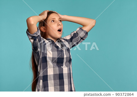 Beautiful teenage girl in a casual checkered shirt is posing against a blue studio background. Beautiful teenage girl in a casual checkered shirt is posing against a blue studio background. 90372864