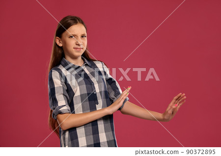 Beautiful teenage girl in a casual checkered shirt is posing against a pink studio background. 90372895