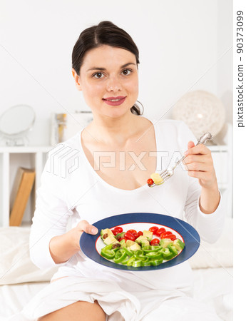 Portrait of brunette lady in white dress eating vegetable salad Portrait of brunette lady in white dress eating vegetable salad 90373099