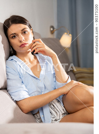 Sad girl sitting on sofa in living room 90373100