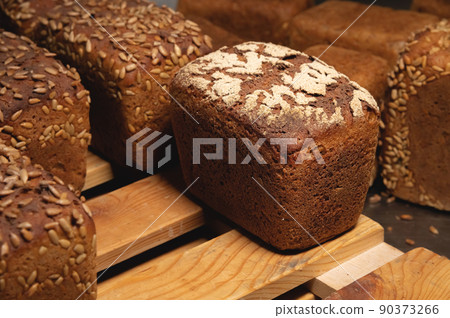 Close-up rye loaves of hot rye bread stand on a wooden tray in a dark bakery room 90373266
