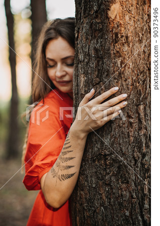 Woman with fern tattoo hugging trees and enjoying nature in the pine forest. 90373496
