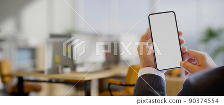 A businessman's hands holding a smartphone mockup over blurred office in the background. 90374554
