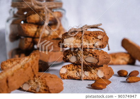 Traditional Italian cantuccini cookies with almonds in glass jar. Sweet dried biscuits. Homemade fresh Italian cookies cantuccini stacks and organic almond seeds. Healthy organic eating 90374947