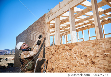 Man worker building wooden frame house. Carpenter using tape measure for measuring wooden planks. Carpentry concept. Man worker building wooden frame house. Carpenter using tape measure for measuring wooden planks. Carpentry concept. 90375784