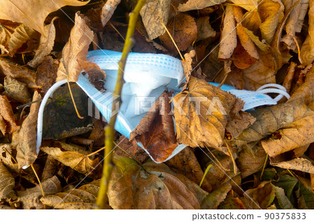 Used medical mask in yellow leaves. The spread of the coronavirus. Protection against Covid-19. The onset of another wave of the virus. Used medical mask in yellow leaves. The spread of the coronavirus. Protection against Covid-19. The onset of another wave of the virus. 90375833