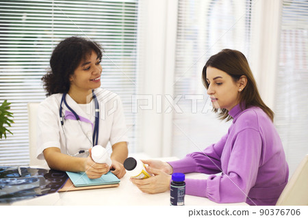 Beautiful young mixed race female doctor with pregnant patient in front of attendee, pill jar holder 90376706