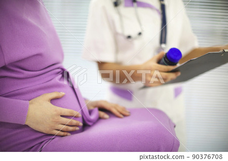 Beautiful young mixed race female doctor with pregnant patient in front of attendee, pill jar holder 90376708