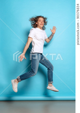 Full-length portrait of young man, student in casual style outfit jumping isolated on blue background. Human emotions, facial expression concept. Trendy colors 90376834