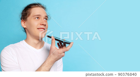 Closeup portrait of young man, student using phone isolated on blue background. Human emotions, facial expression concept. Trendy colors 90376840