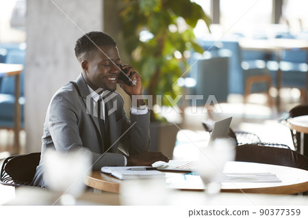 Happy excited young black businessman in formal suit sitting at table with laptop in cafe Happy excited young black businessman in formal suit sitting at table with laptop in cafe 90377359