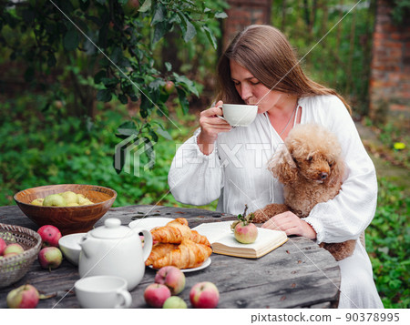 woman enjoying morning coffee in apple orchard with her pet poodle woman enjoying morning coffee in apple orchard with her pet poodle 90378995