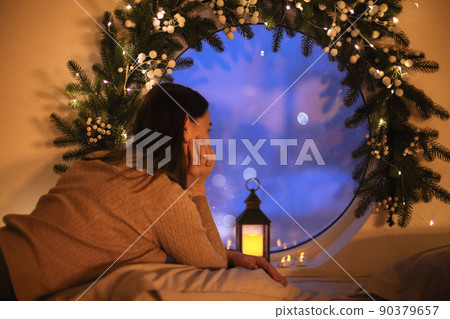 Dreamy woman looking out round window on Christmas Eve at home 90379657