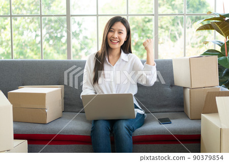 Happy young Asian woman entrepreneur, Smile for sales success after checking order from online shopping store in laptop at home office, Concept of merchant business online and eCommerce 90379854