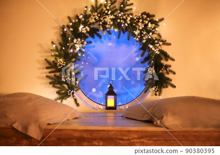Christmas time. Vintage glowing lantern by round window decorated with tree branch and xmas lights Christmas time. Vintage glowing lantern by round window decorated with tree branch and xmas lights 90380395