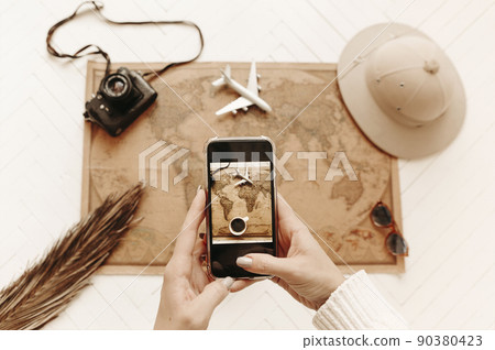 Top view of female hands with smartphone making photo from above of vintage looking world map 90380423