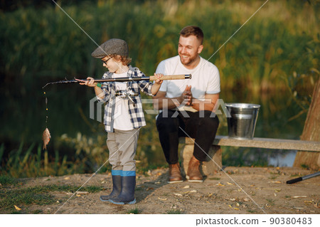 Young dad and his child boy spend time outdoors together. Curly toddler boy wearing a plaid shirt and a hat. Boy sitting near the tree and listening his father. Young dad and his child boy spend time outdoors together. Curly toddler boy wearing a plaid shirt and a hat. Boy sitting near the tree and listening his father. 90380483