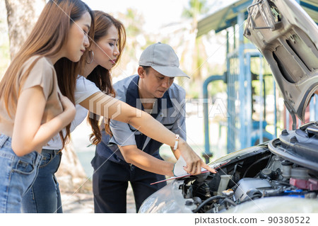 Asian male auto mechanic holds a clipboard and examines car engine breakdown problem with women customer and explain the root cause and estimate repair quotation, Car repair, and maintenance concept. 90380522