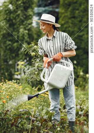 Gardening in summer. Woman watering flowers with a watering can. Girl wearing a hat. Gardening in summer. Woman watering flowers with a watering can. Girl wearing a hat. 90380624