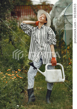Gardening in summer. Woman watering flowers with a watering can. Girl wearing a hat. Gardening in summer. Woman watering flowers with a watering can. Girl wearing a hat. 90380633