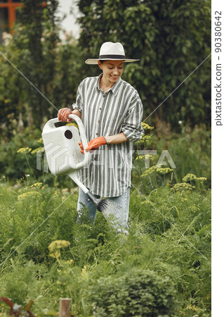 Gardening in summer. Woman watering flowers with a watering can. Girl wearing a hat. Gardening in summer. Woman watering flowers with a watering can. Girl wearing a hat. 90380642