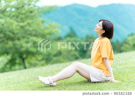 一位年輕女子坐在新鮮綠色公園的草地上,令人耳目一新 一位年輕女子坐在新鮮綠色公園的草地上,令人耳目一新 90382188