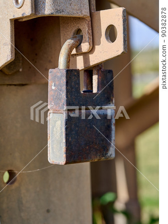 The gate is closed with a rusty padlock. Object security. The gate is closed with a rusty padlock. Object security. 90382878