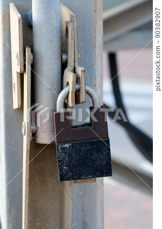The gate is closed with a rusty padlock. Object security. The gate is closed with a rusty padlock. Object security. 90382907