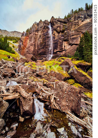 Gigantic waterfall over vertical cliffs leading to boulders of moss in valley 90383415
