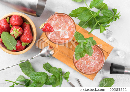 Cold strawberry cocktail mojito, margarita, daiquiri in two glasses with mint, ice and bartender tools on light table Cold strawberry cocktail mojito, margarita, daiquiri in two glasses with mint, ice and bartender tools on light table 90385231